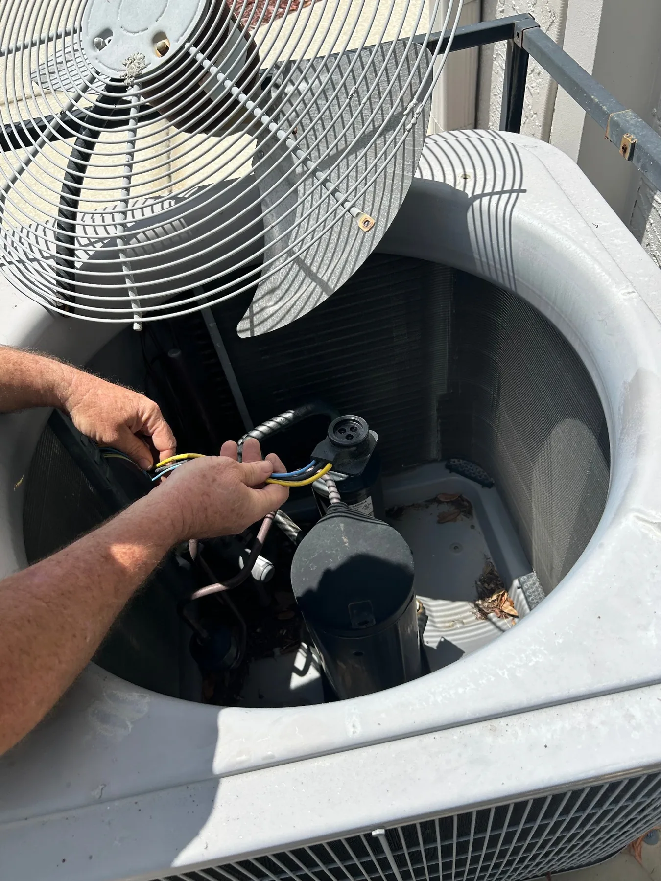 Technician servicing electrical components inside an outdoor air conditioner